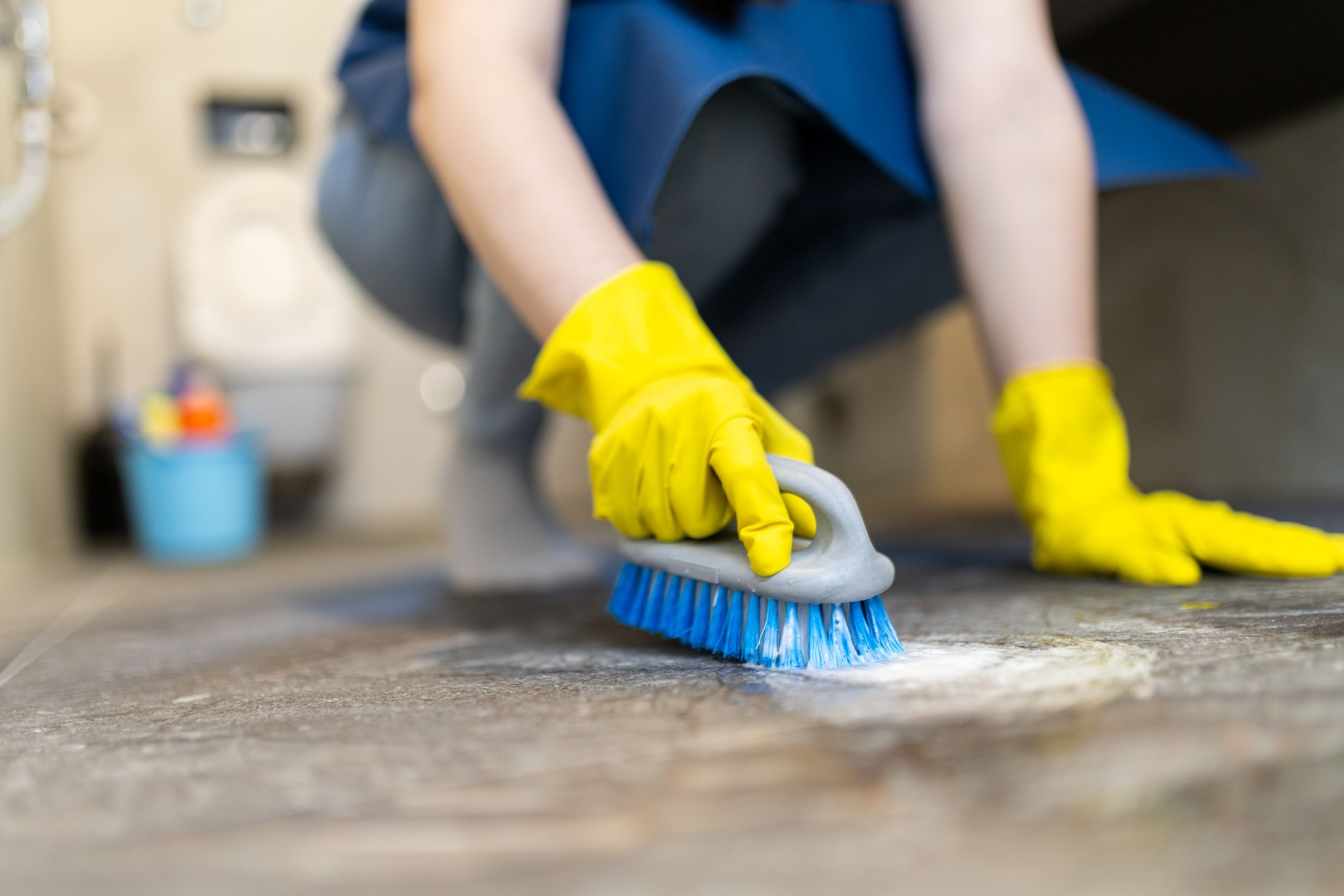 Individual scrubbing floor with brush while wearing yellow gloves in a clean environment